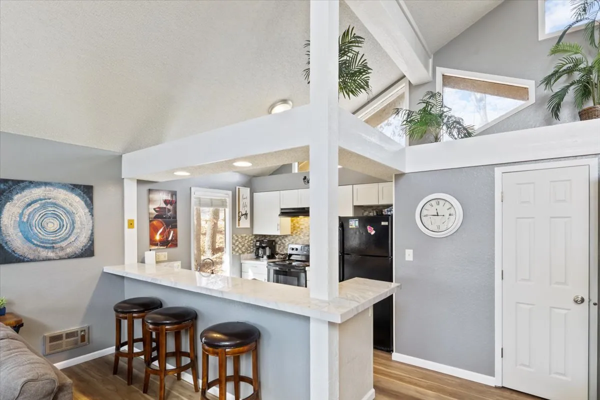 An inviting interior scene showing a stylish bar counter and kitchen area, illuminated by natural light from skylights. The area is set for entertaining, cooking, and relaxing, with tasteful wall art enhancing the homey, yet upscale, vibe.