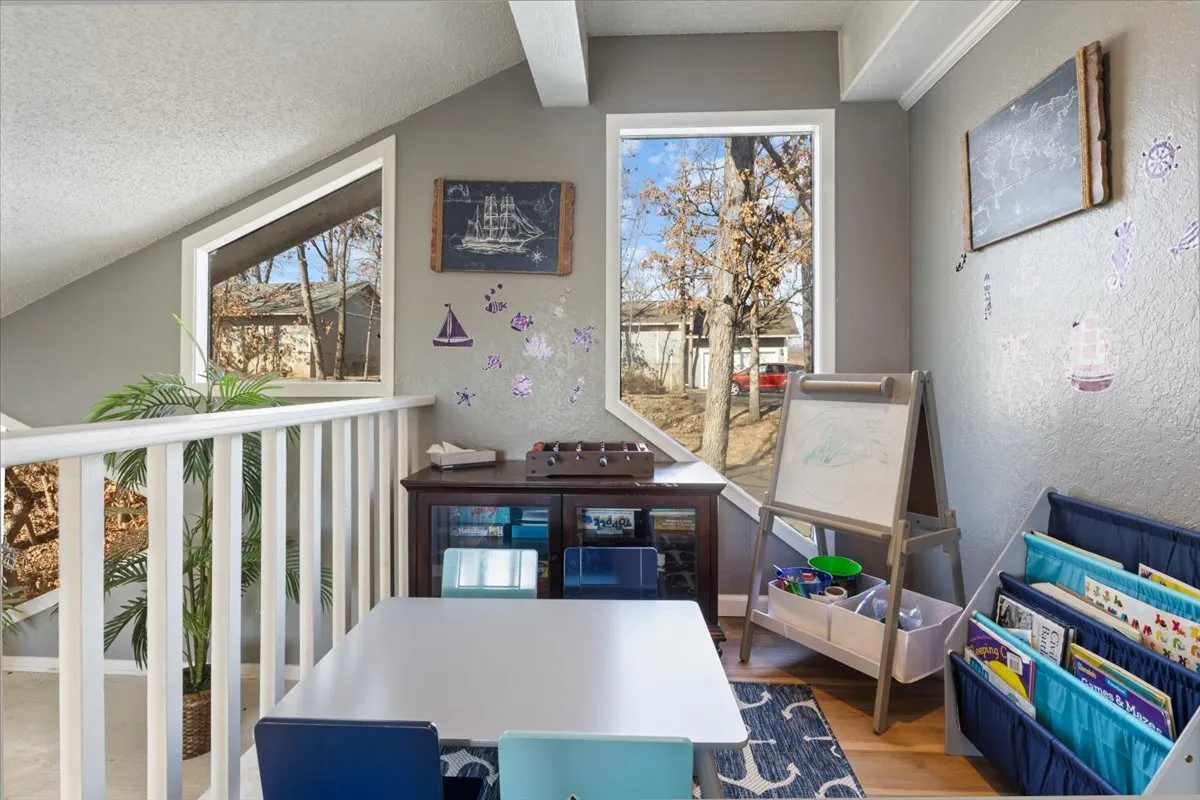 A vibrant, multifunctional area with a central table surrounded by chairs, colorful storage for games and books, an art easel, and creative wall decor. The room encourages playful activities, reading, and creative gatherings.