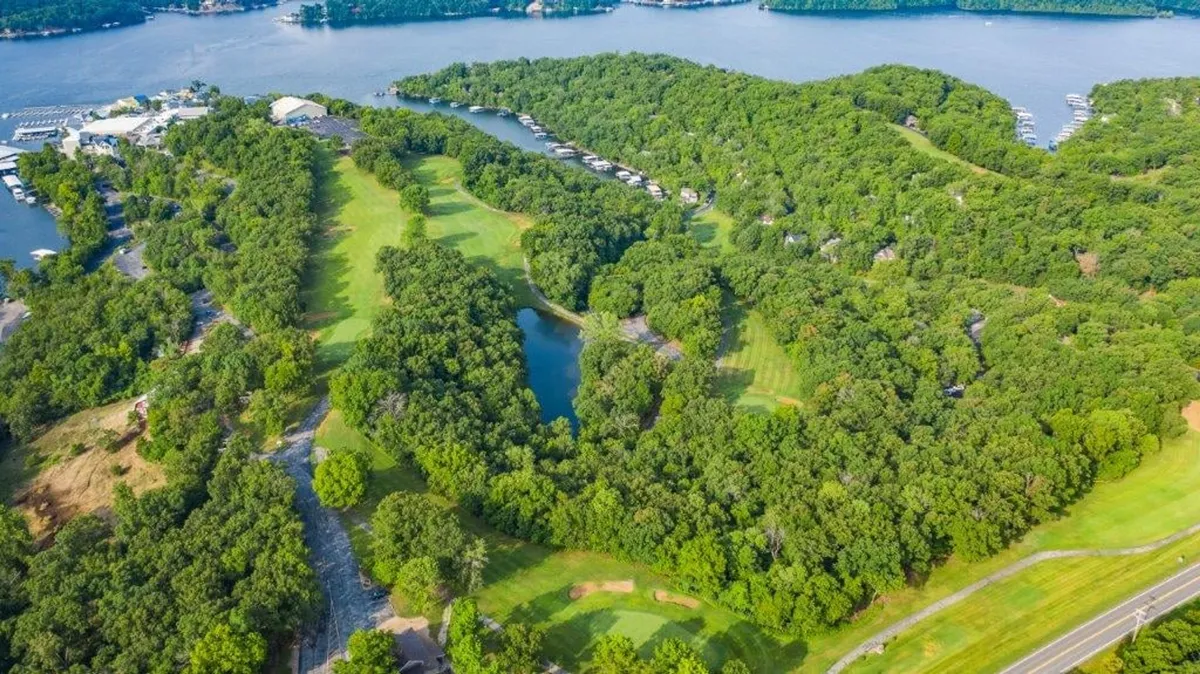A sweeping exterior view of lush greenery, a well-manicured golf course, the lake, and a marina, all set under an expansive sky.