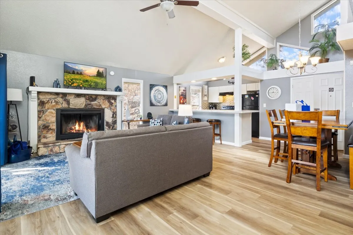 A warm, open-concept living and dining room highlighted by a central fireplace. The space features a cozy sofa, a large dining table ideal for family meals, and tasteful artwork on the walls. Natural light fills the room, and the inviting arrangement encourages both relaxation and group gatherings.