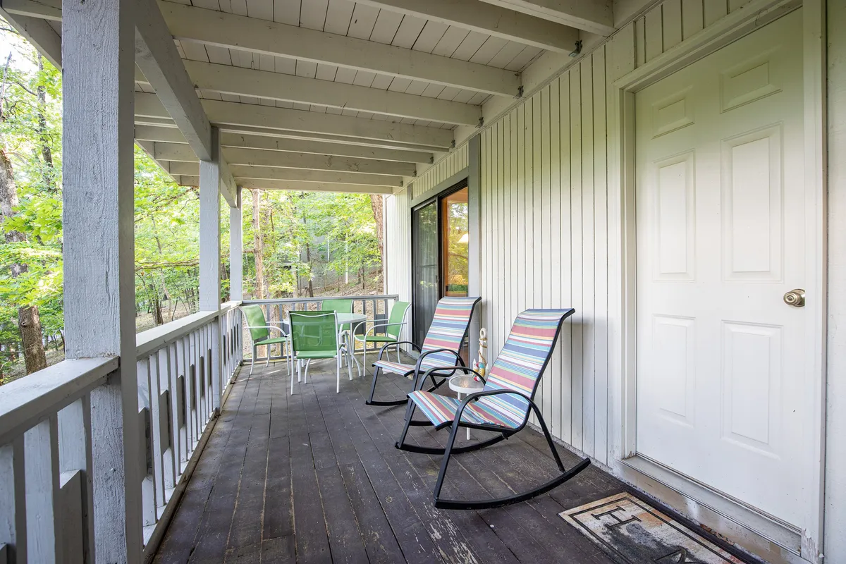 The image showcases a serene outdoor dining area with rocking chairs and a table, bordered by trees. The setup encourages relaxation, socializing, and shared meals in nature’s embrace.